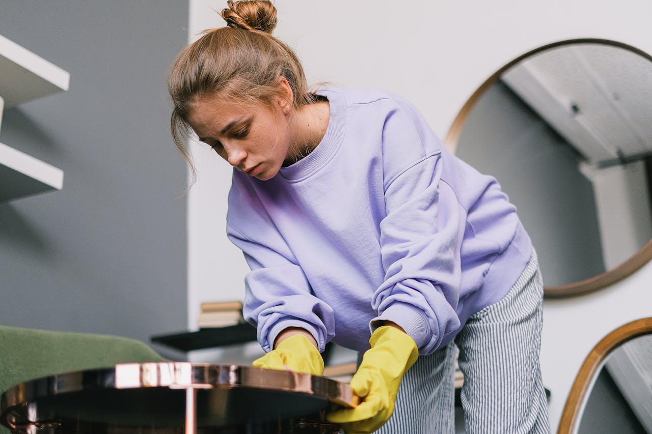From below of young female in casual clothes and latex gloves standing and wiping table against mirrors in light room in daytime
